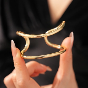 Gros plan d'un bracelet jonc doré à double couche sur la main d'un mannequin, fond sombre