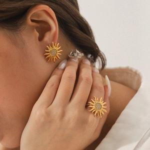 Close-up of gold sun-shaped stud earrings and ring set with crystals on a model