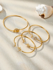 Détail de quatre bracelets dorés thème océan avec étoiles de mer et coquillages sur sable