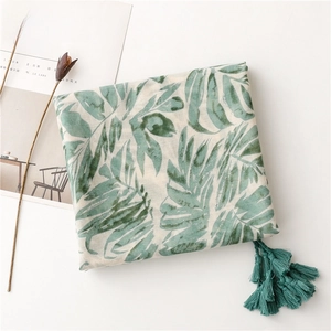 Detail of green tropical leaf pattern scarf with dark green tassel charms on a white table