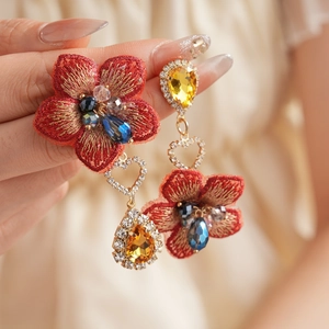 Gros plan sur boucles d'oreilles fleurs en tissu rouge avec cœur en cristal et goutte d'or