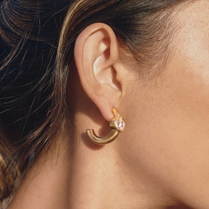 Close-up of gold-plated C-shaped earrings with a heart-shaped zircon stone inlay