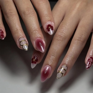 Detail of burgundy press-on nails with gold accents and hand-painted floral art
