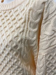 Gros plan d'un pull en maille torsadée crème montrant la texture et le col roulé détaillé