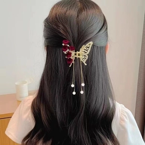 Elegant gold butterfly hair claw clip with red floral accents and pearl tassels on a woman