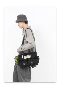 Detail of black crossbody messenger bag featuring multi-pocket design and dinosaur charm