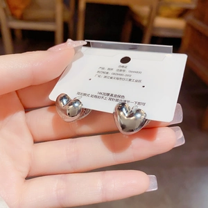 Detail of hollow heart-shaped earrings in polished silver finish with secure hoop closure