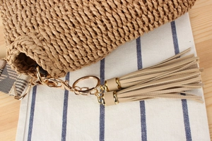 Detailed close-up of woven straw bag texture with golden hardware and leather tassels
