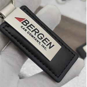 Close-up of black leather keychain with engraved silver metal plate held by hand