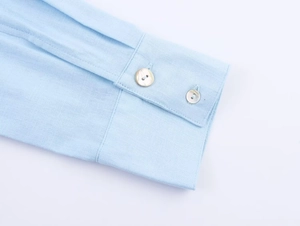Detailed close-up of light blue linen shirt cuff with two pearl texture buttons
