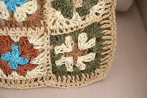 Macro detail of colorful crochet granny square pattern on a woven straw bag