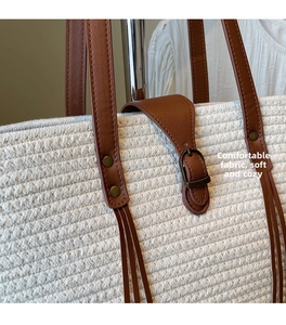 Close-up of cream woven straw tote bag with brown leather handles and metal rivets