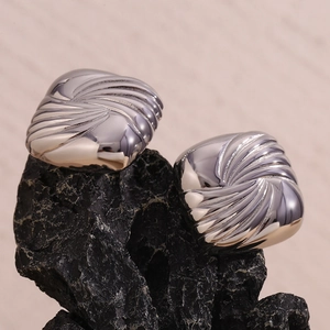 Macro shot of silver square earrings with spiral wave texture on dark mineral stone