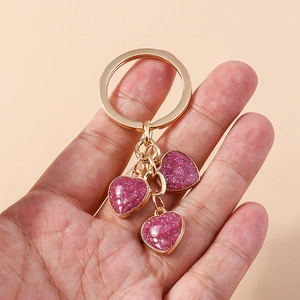 Detailed view of three glittery pink heart charms on a gold-plated keychain holder