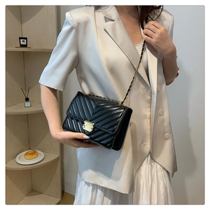 Close-up of black quilted chain bag with elegant gold lock and leather strap detail