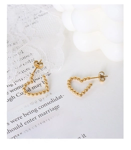 Macro detail of gold beaded heart earrings on white lace and elegant background