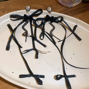Détail de boucles d'oreilles nœuds noirs avec pompons en strass et perles blanches