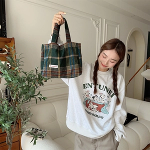 Detail of green plaid wool tote bag showing texture and woven label with a cozy interior background