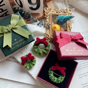 Macro shot of green velvet Christmas wreath brooches in red and green gift boxes