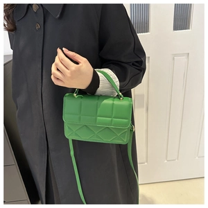 Detail of green PU leather crossbody bag with rhombic pattern and top handle worn by a model