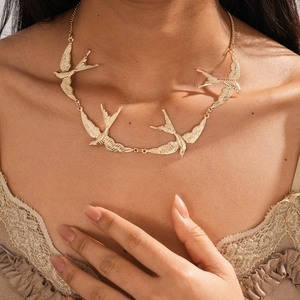 Nahaufnahme der goldenen Schwalben-Halskette mit Metallic-Finish am Modell