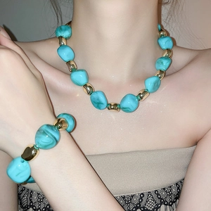 Close-up of turquoise and gold beaded necklace and bracelet set on a female model