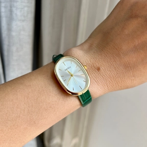 Elegant women's quartz watch featuring a gold oval case and green leather strap on wrist