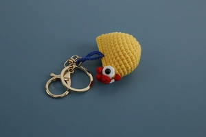 Close-up of handmade yellow knitted chicken keychain with golden metal hook and blue cord
