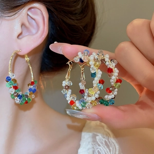 Close-up of pearl and colorful crystal hoop earrings worn on ear with golden finish
