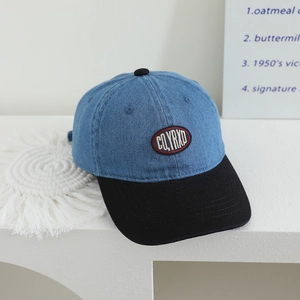Detail of color-block kids denim baseball cap with CLYRXD embroidery on a white pedestal