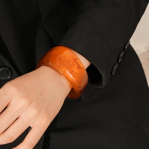 Detailed macro view of wide amber resin bangle with unique marbled patterns on black blazer