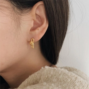 Close-up of minimalist gold knot stud earrings worn by a model in a soft setting