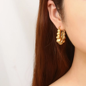 Close-up of model wearing gold C-shaped hoop earrings with textured bubble design