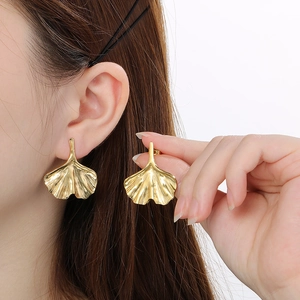 Detail view of golden ginkgo leaf earrings with realistic vein texture on a model