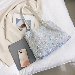 Large sequin tote bag with iridescent finish styled on bed with tablet and blazer