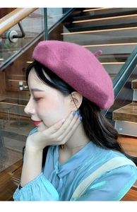Close-up of a stylish plum purple wool beret worn by a model in a modern indoor setting