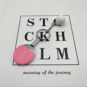 Close-up of a pink mini table tennis paddle keychain and ball on a white prop card