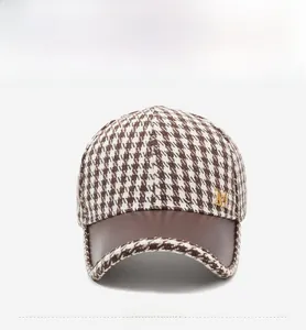 Detail of houndstooth baseball cap featuring brown leather brim and metal M logo