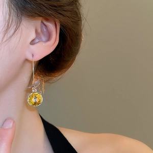 Close-up of dangling silver leaf earrings with a large faceted yellow zircon on a model