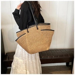 Detail of straw woven tote bag featuring wide black leather shoulder straps and side pocket