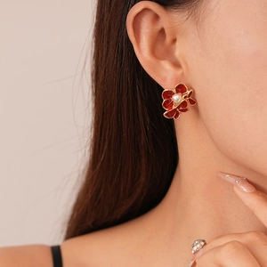 Close-up of red enamel flower stud earring with a white pearl on a female model