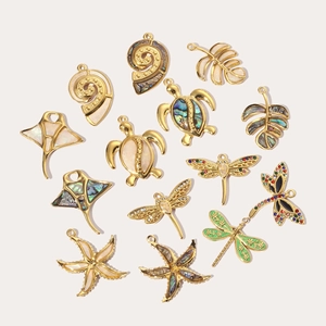 Flat lay of gold-plated ocean charms with dragonfly and seashell inlays on cream background