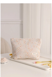 Detail of tweed makeup bag on white tray with brushes and floral background