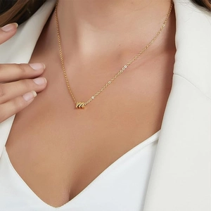 Close-up of a model wearing a gold lowercase letter m necklace against a white outfit