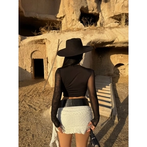 Detail of sheer mesh patchwork sleeves on a sexy black crop top with white textured skirt