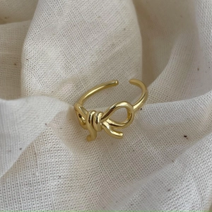Detailed view of a gold-plated bow-knot adjustable ring on a rustic linen fabric surface