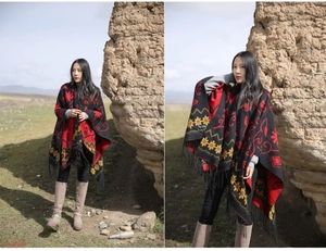 Detailed view of ethnic wool shawl with red yellow patterns and tassels on black fabric