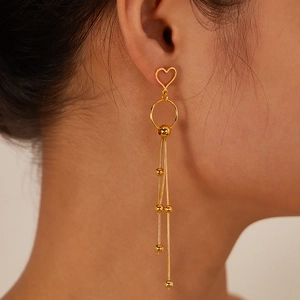 Detail showing elegant gold tassel earrings with hollow heart studs worn by a model