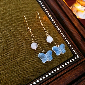 Macro detail of butterfly tassel earring with blue glass pendant on vintage frame