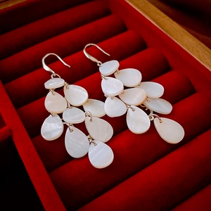 Macro view of tiered teardrop mother-of-pearl earrings on a premium velvet background